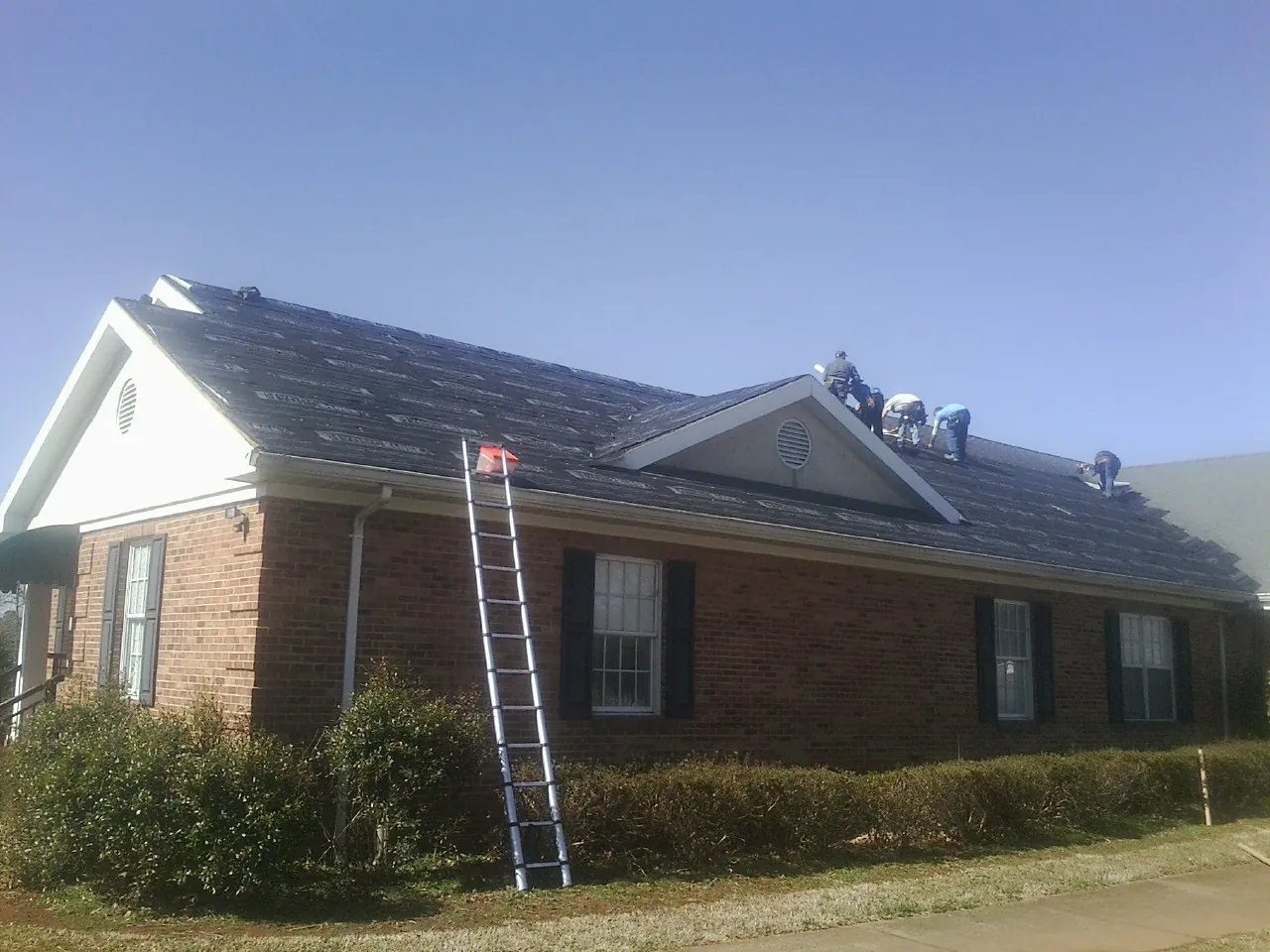 Crew tearing shingles off a brick ranch roof with a ladder set — Emergency Roof Repair work by our crew in Ronks