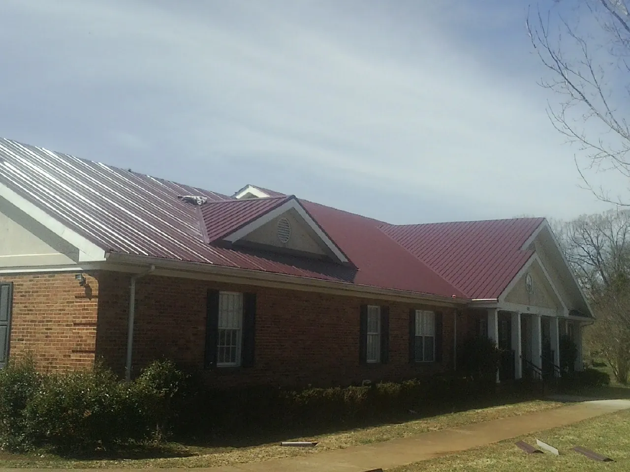 Red metal roof with gabled entries on a long brick building, from a Hail Damage Roof Repair job in Ronks
