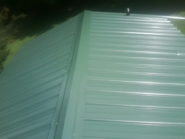 New green metal panels meeting at the ridge of a roof — Flat Roof Repair work by our crew in Ronks