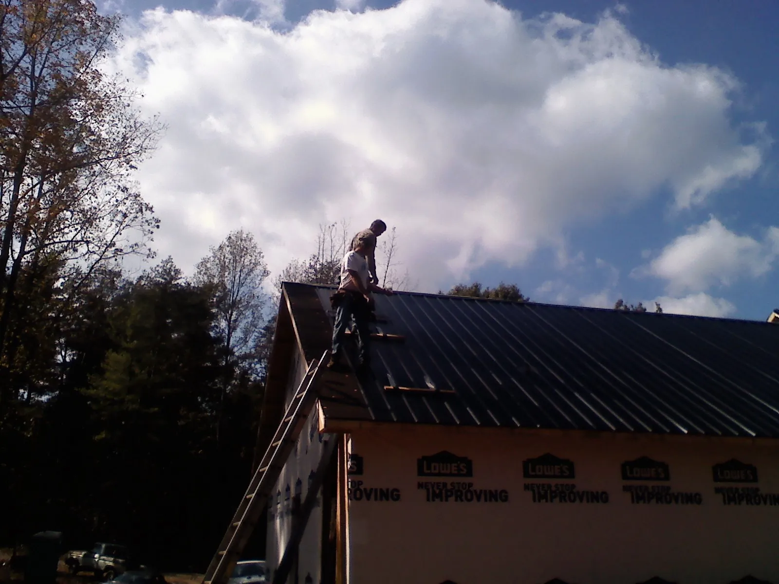 Roofer fastening dark metal panels high against a cloudy sky, from a Roof Inspection job in Ronks