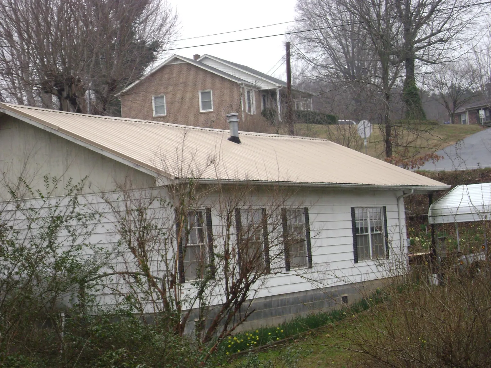 Tan metal roof on a white sided house set into a hillside — Commercial Roofing by Roofing Brothers in Ronks